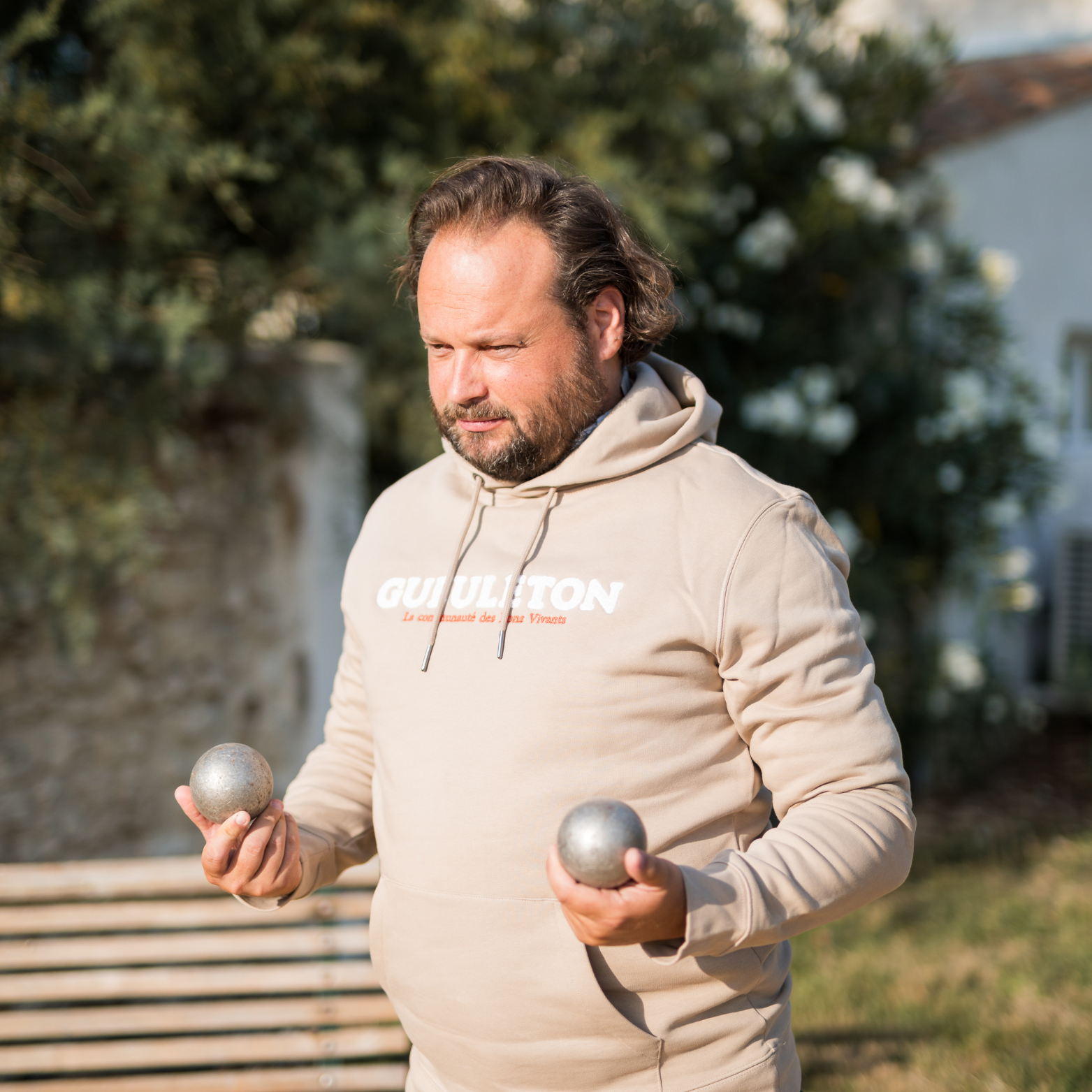 Sweat à capuche Gueuleton unisex Beige porté par un homme jouant à la pétanque - Gueuleton