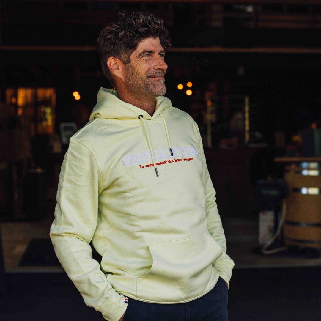 homme portant un sweat à capuche jaune Gueuleton avec le logo 'La communauté des Bons Vivants', style décontracté et convivial