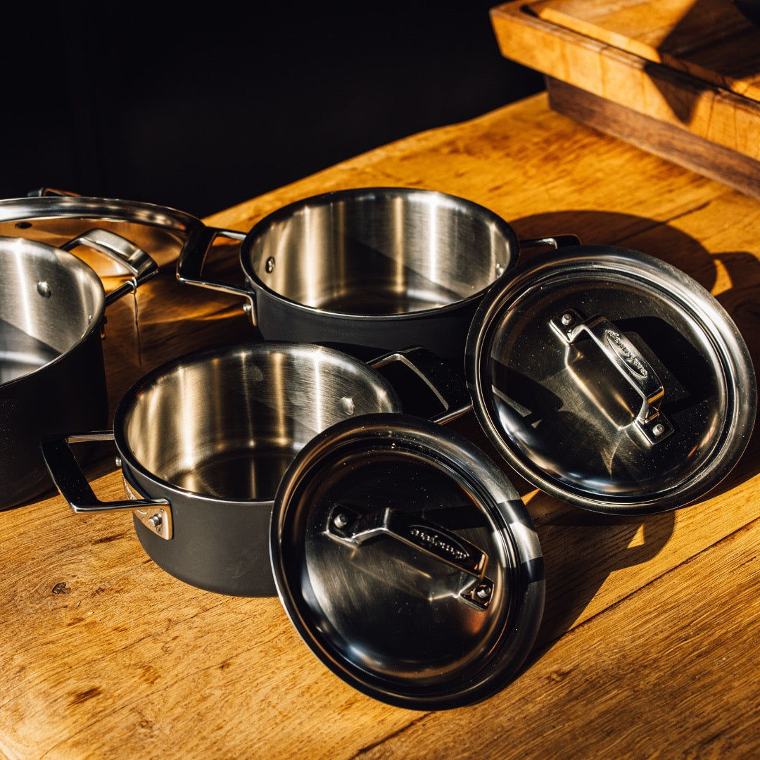 Cocottes en inox brossé Demeyere avec couvercles, posées sur une table en bois dans une lumière dorée