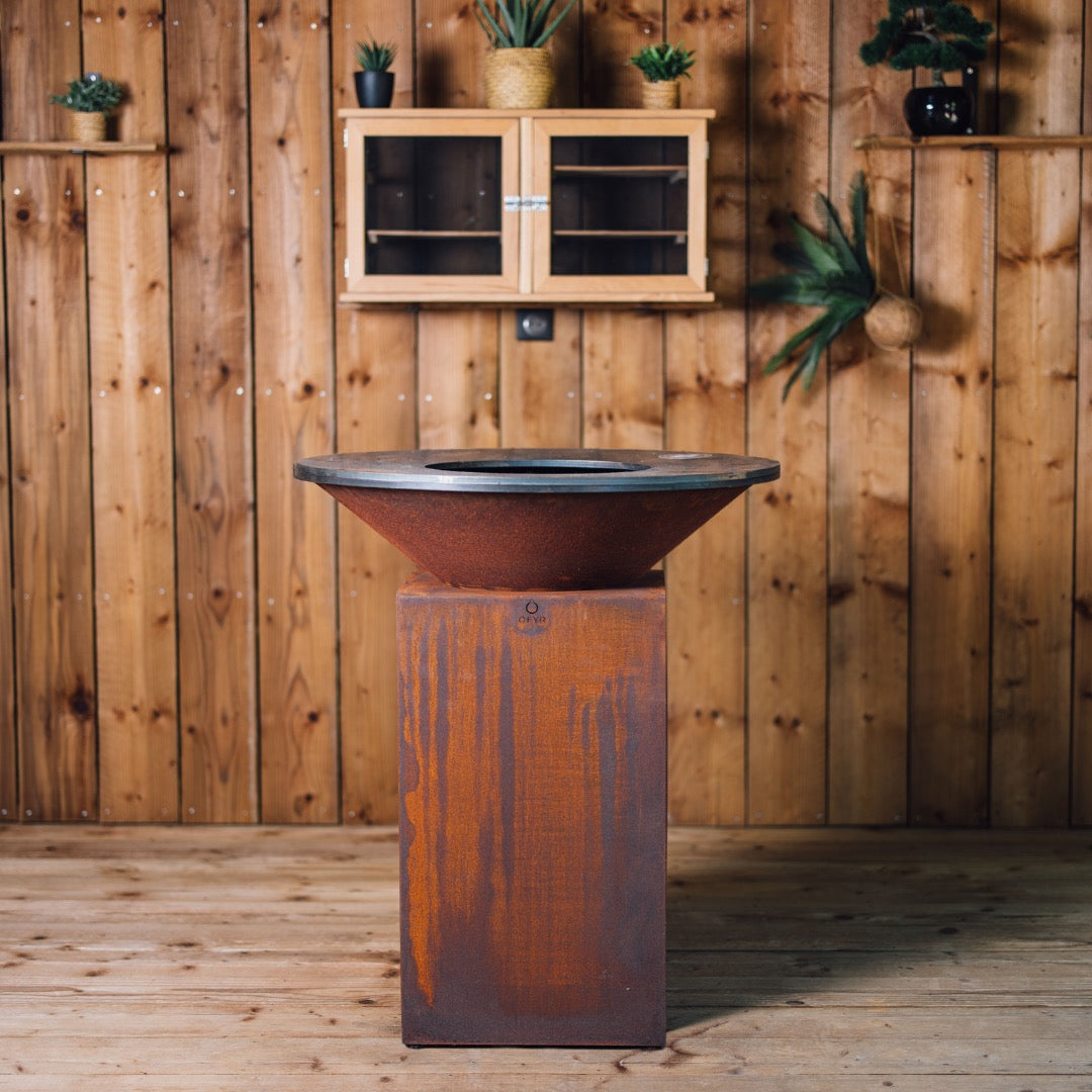Vue arrière du Brasero Classic Corten 85 en acier patiné, avec sa base droite et son foyer circulaire, dans un décor en bois naturel.