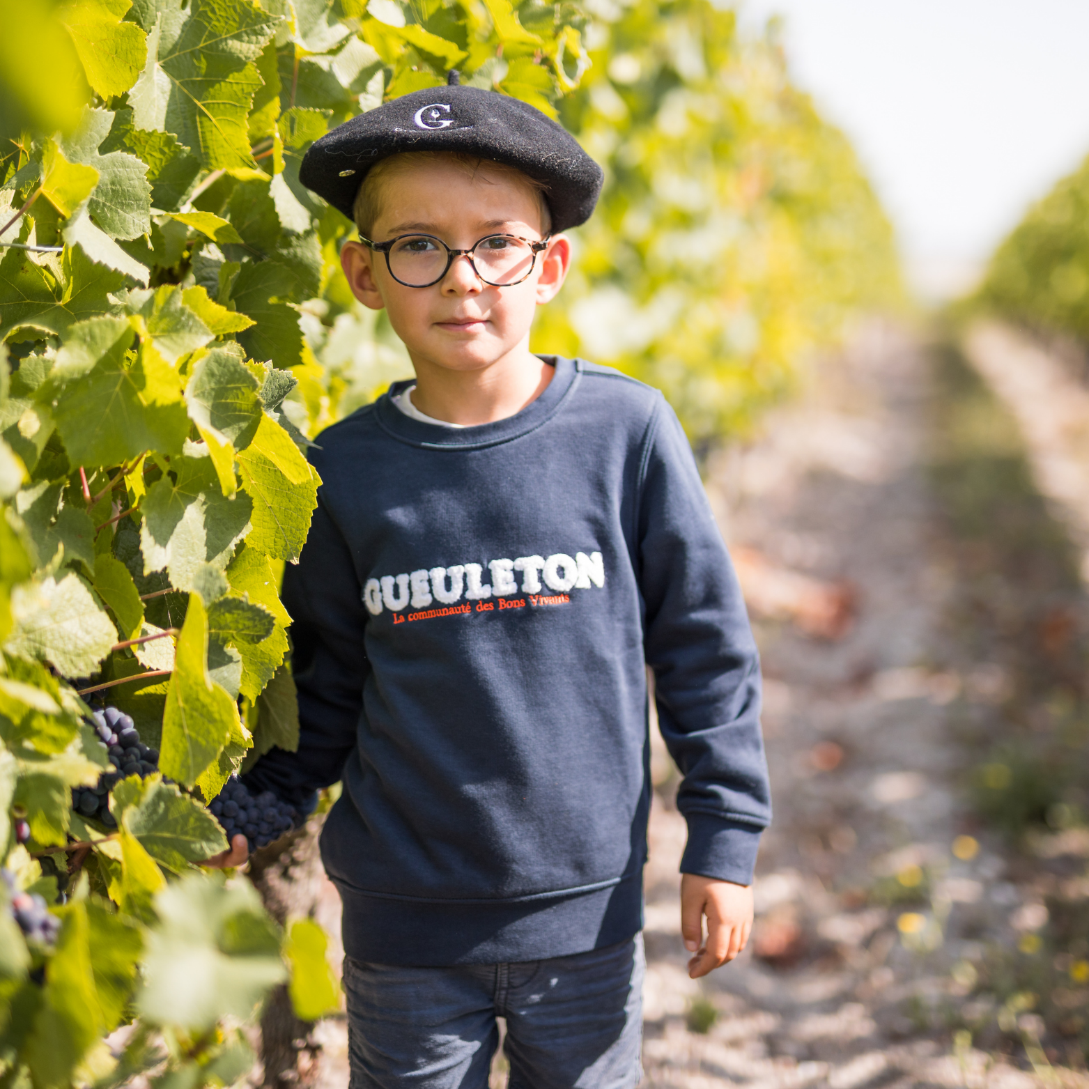 Enfant portant un sweat Gueuleton Marine et un béret dans les vignes - Gueuleton