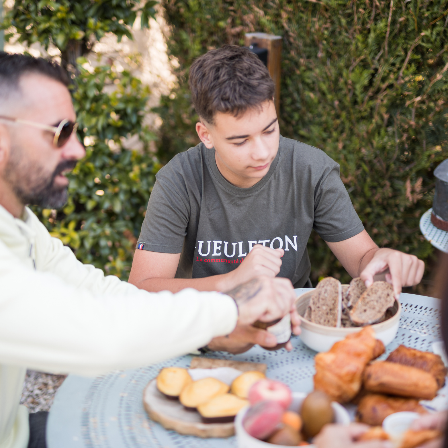 T-shirt Gueuleton Vert Kaki porté par un jeune homme autour d'une table avec du pain - Gueuleton