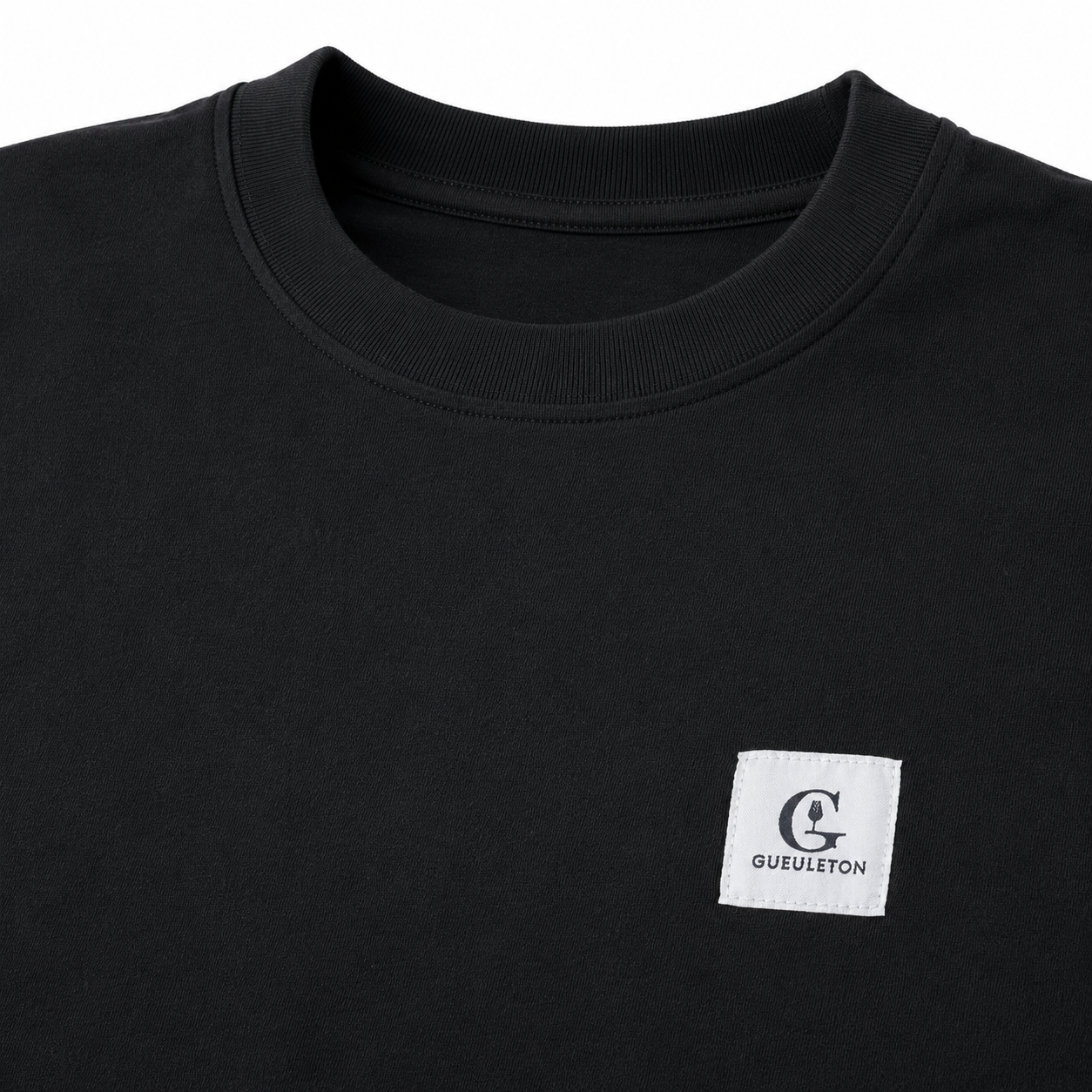 Gros plan patch tissé Gueuleton sur t-shirt noir coton bio 180g, col rond, fond blanc